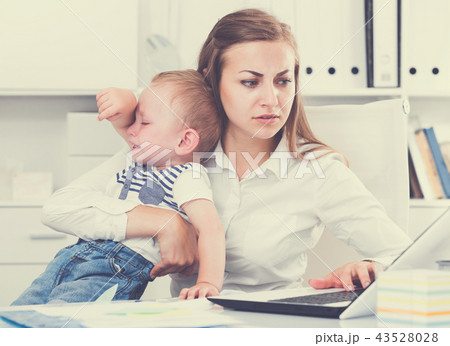 Female is working with a naughty kid in her arms behind a laptop 43528028
