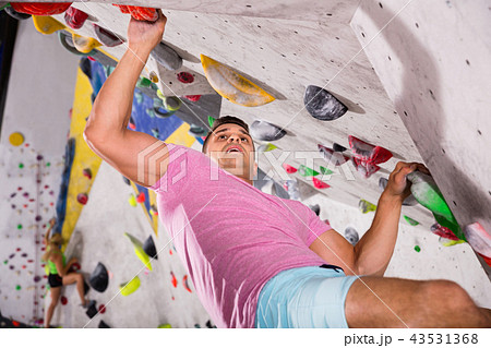 Male alpinist practicing indoor rock-climbing on artificial boulder without safety belts 43531368