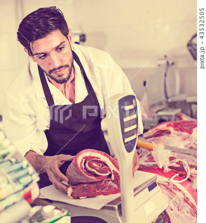 Adult male butcher in uniform is weighing meat Adult male butcher in uniform is weighing meat 43532505