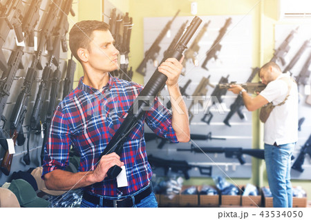 Young cheerful male is choosing air-powered gun Young cheerful male is choosing air-powered gun 43534050