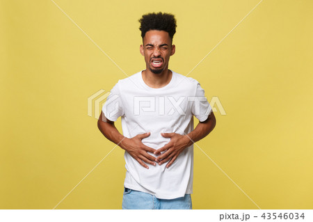 Closeup portrait of miserable, upset, young man, doubling over in stomach pain, looking very sick Closeup portrait of miserable, upset, young man, doubling over in stomach pain, looking very sick 43546034