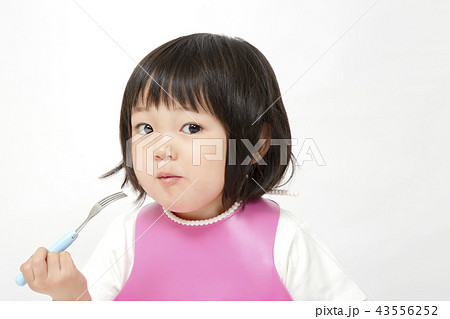 白バックでフォークを手に持ち食事中の幼い女の子 子供の健康 成長 食事 育児イメージの写真素材