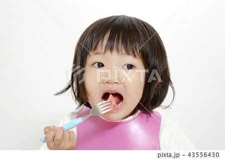 白バックでフォークに刺したスイカを食べている幼い女の子 子供の健康 成長 育児 おやつイメージの写真素材