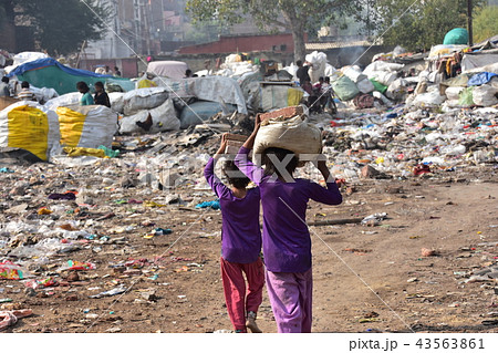 インドの首都 デリーのスラム レンガを頭に乗せて運ぶインド人少女 バラックの住居とゴミ集積所の写真素材