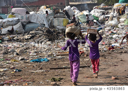 インドの首都 デリーのスラム レンガを頭に乗せて運ぶインド人少女 バラックの住居とゴミ集積所の写真素材