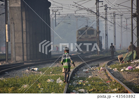 インドの首都デリー 線路沿いのスラム 線路を歩いて遊ぶ少年 遠くから近付くインド鉄道 インドの首都デリー 線路沿いのスラム 線路を歩いて遊ぶ少年 遠くから近付くインド鉄道 43563892