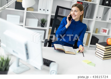 A young girl is sitting at a computer desk, holding a yellow marker in her hand and talking on the 43615724