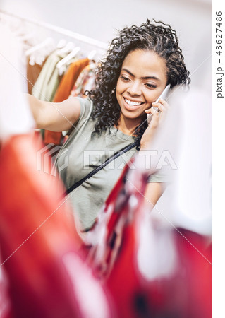 Smiling woman speaking on phone in clothing shop Smiling woman speaking on phone in clothing shop 43627486