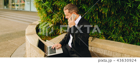 Manager talking by smartphone and working with laptop outside in 43630924