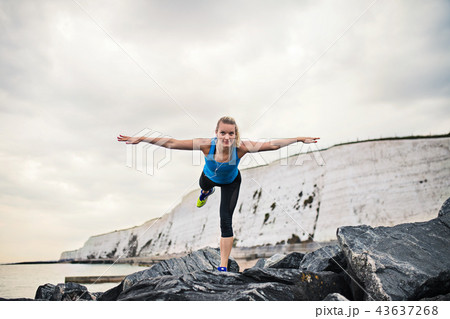 Young sporty woman runner with earphones stretching on the beach outside. 43637268
