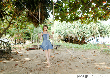 Young european woman wearing jeans dress and riding on swing, sand in background. 43663599