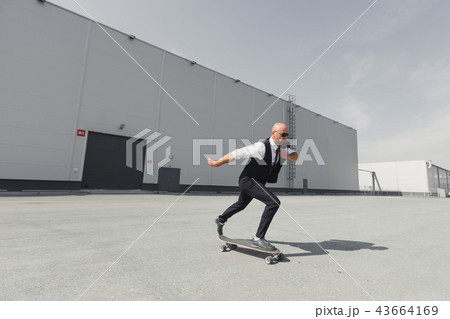Confident young businessman in business suit on longboard hurrying to his office, on the street in Confident young businessman in business suit on longboard hurrying to his office, on the street in 43664169