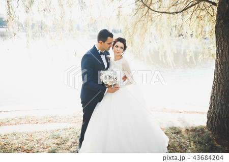 Stylish couple of happy newlyweds walking in the park on their wedding day with bouquet Stylish couple of happy newlyweds walking in the park on their wedding day with bouquet 43684204