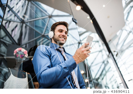 A young businessman with smartphone and headphones in a modern building. A young businessman with smartphone and headphones in a modern building. 43690411