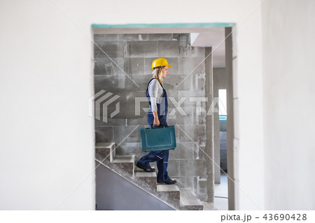 Woman worker with a tool box walking down the stairs on the construction site. Woman worker with a tool box walking down the stairs on the construction site. 43690428