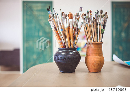 A bunch of art brushes standing in ceramic vases, on the table in the art studio A bunch of art brushes standing in ceramic vases, on the table in the art studio 43710063