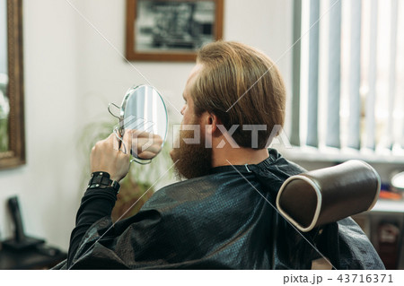 Handsome young bearded guy sitting in an armchair in a beauty salon Handsome young bearded guy sitting in an armchair in a beauty salon 43716371