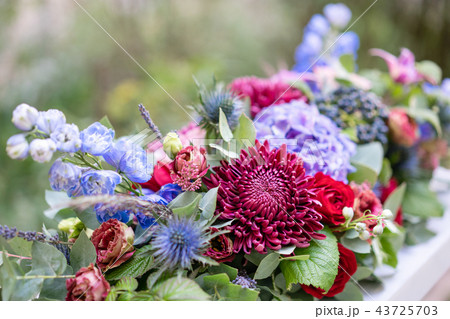 Elongated floral arrangement in vintage metal vase. table setting. Blue and red color. Gorgeous Elongated floral arrangement in vintage metal vase. table setting. Blue and red color. Gorgeous 43725703