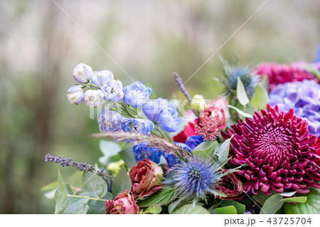 Elongated floral arrangement in vintage metal vase. table setting. Blue and red color. Gorgeous Elongated floral arrangement in vintage metal vase. table setting. Blue and red color. Gorgeous 43725704