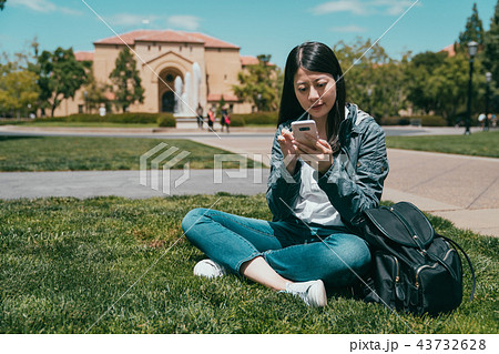 student checking on phone and sitting on grass 43732628