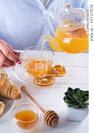 The woman's hands pour sea buckthorn tea on a table with honey and croissants The woman's hands pour sea buckthorn tea on a table with honey and croissants 43737639