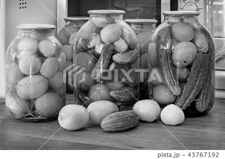 Canned tomatoes and cucumbers in large glass jars. Black-and-white image. Canned tomatoes and cucumbers in large glass jars. Black-and-white image. 43767192