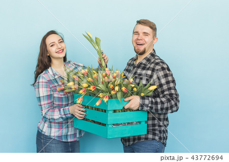 Happy man and woman florists holding box with tulips and laughing on blue background Happy man and woman florists holding box with tulips and laughing on blue background 43772694