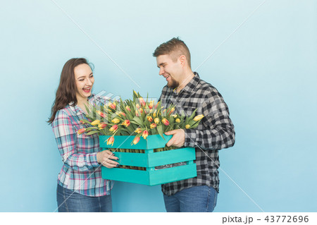 Happy man and woman florists holding box with tulips and laughing on blue background Happy man and woman florists holding box with tulips and laughing on blue background 43772696