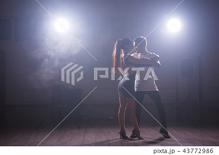 Skillful dancers performing in the dark room under the concert light and smoke. Sensual couple Skillful dancers performing in the dark room under the concert light and smoke. Sensual couple 43772986