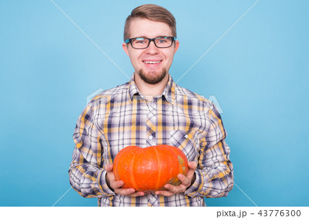 People, holidays and autumn concept - handsome man holding pumpkins on blue background 43776300