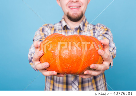 Close up of smiling man holding pumpkins over blue background, harvest concept 43776301
