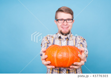 Close up of smiling man holding pumpkins over blue background, harvest concept Close up of smiling man holding pumpkins over blue background, harvest concept 43776303