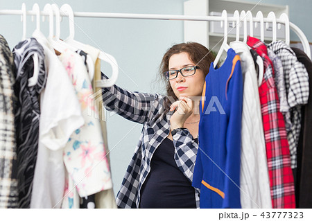 Clothes, fashion, people concept - serious young woman choosing clothes in her wardrobe 43777323