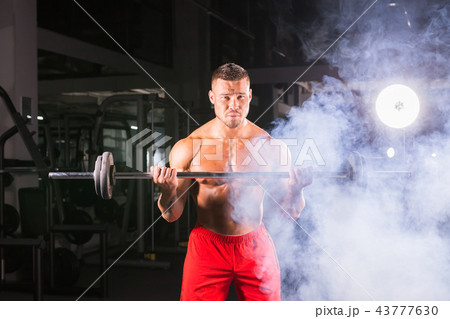 Bodybuilder doing the exercises with barbell. Strong male with naked torso on dark background 43777630