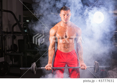 Muscular young man lifting weights in gym Muscular young man lifting weights in gym 43777631