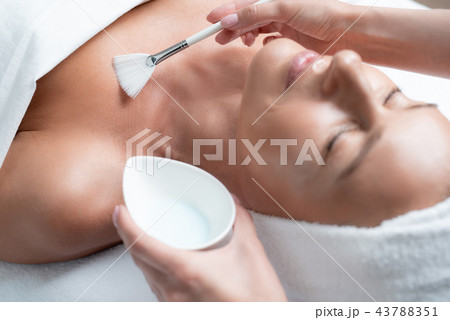 Beautician using cosmetic brush for applying mask on woman skin Beautician using cosmetic brush for applying mask on woman skin 43788351