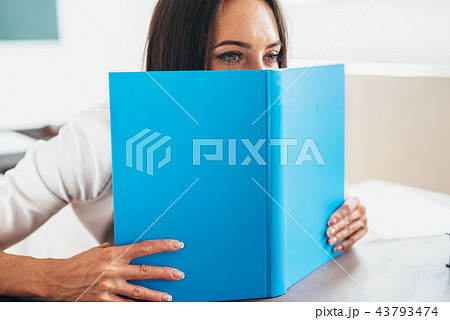 Female student hiding behind an open book Female student hiding behind an open book 43793474