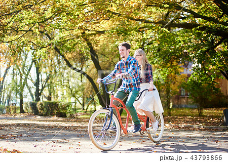 Young couple, handsome man and attractive woman on tandem bike in sunny summer park or forest. Young couple, handsome man and attractive woman on tandem bike in sunny summer park or forest. 43793866