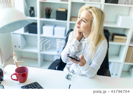 A young girl in the office sits at a desk holding a phone in her hand and talking on it through a 43796704