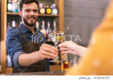 Cheerful barman smiling to the client while giving glass of alcohol Cheerful barman smiling to the client while giving glass of alcohol 43834307