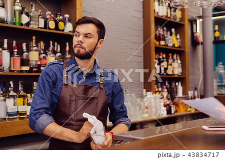 Curious barman thoughtfully looking into the distance while cleaning glasses Curious barman thoughtfully looking into the distance while cleaning glasses 43834717