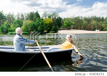 Happy aged woman touching water and her husband rowing the boat Happy aged woman touching water and her husband rowing the boat 43836231