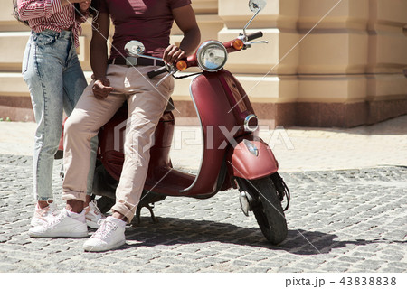 Romantic Relationship. Young diverse couple sitting on bike on the city street legs close-up Romantic Relationship. Young diverse couple sitting on bike on the city street legs close-up 43838838
