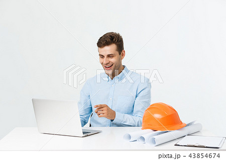 Handsome male engineer is using a notebook for work. He is sitting at the desk and smiling. Copy 43854674