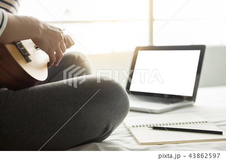 Happy young asian woman playing ukulele sitting on bed in bedroo Happy young asian woman playing ukulele sitting on bed in bedroo 43862597