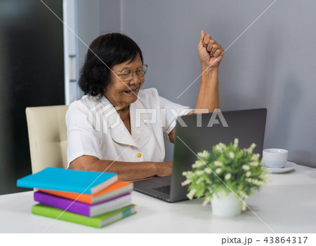 successful senior woman working on laptop with arms raised successful senior woman working on laptop with arms raised 43864317
