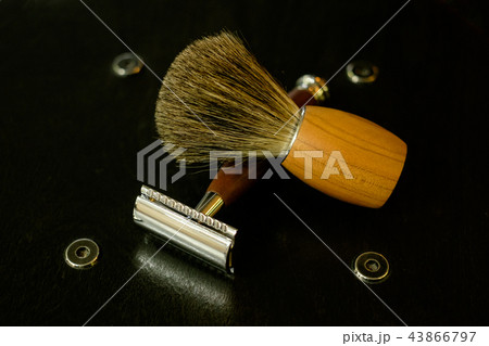 A traditional steel razor with a brown handle of precious wood and a shaving brush on a natural wood A traditional steel razor with a brown handle of precious wood and a shaving brush on a natural wood 43866797