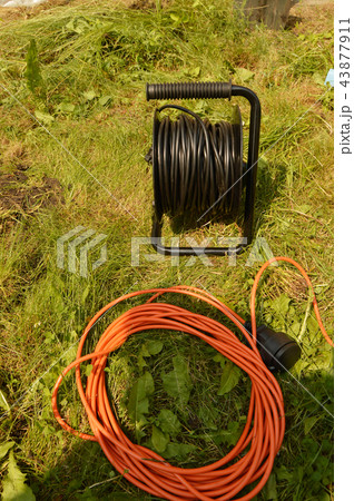 Coil with electric cable and extension cord on the grass, electric tools for construction works in 43877911
