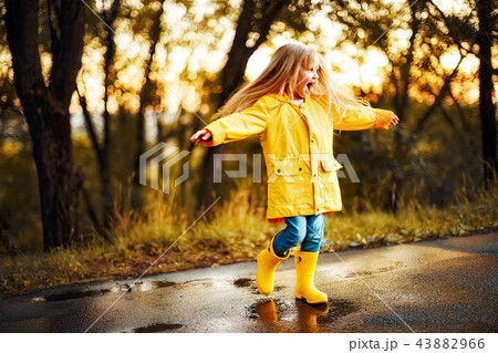 happy child girl in yellow coat anmd rubber boots jumping in puddle 43882966