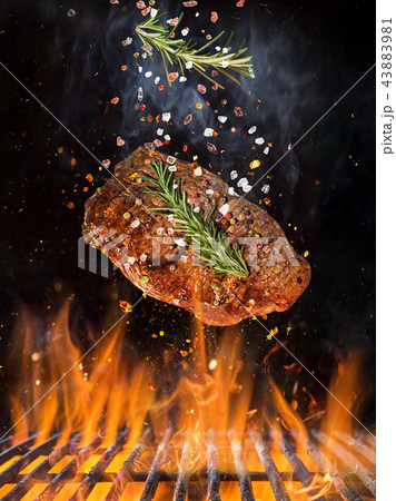 Tasty beef steak flying above cast iron grate with fire flames. 43883981